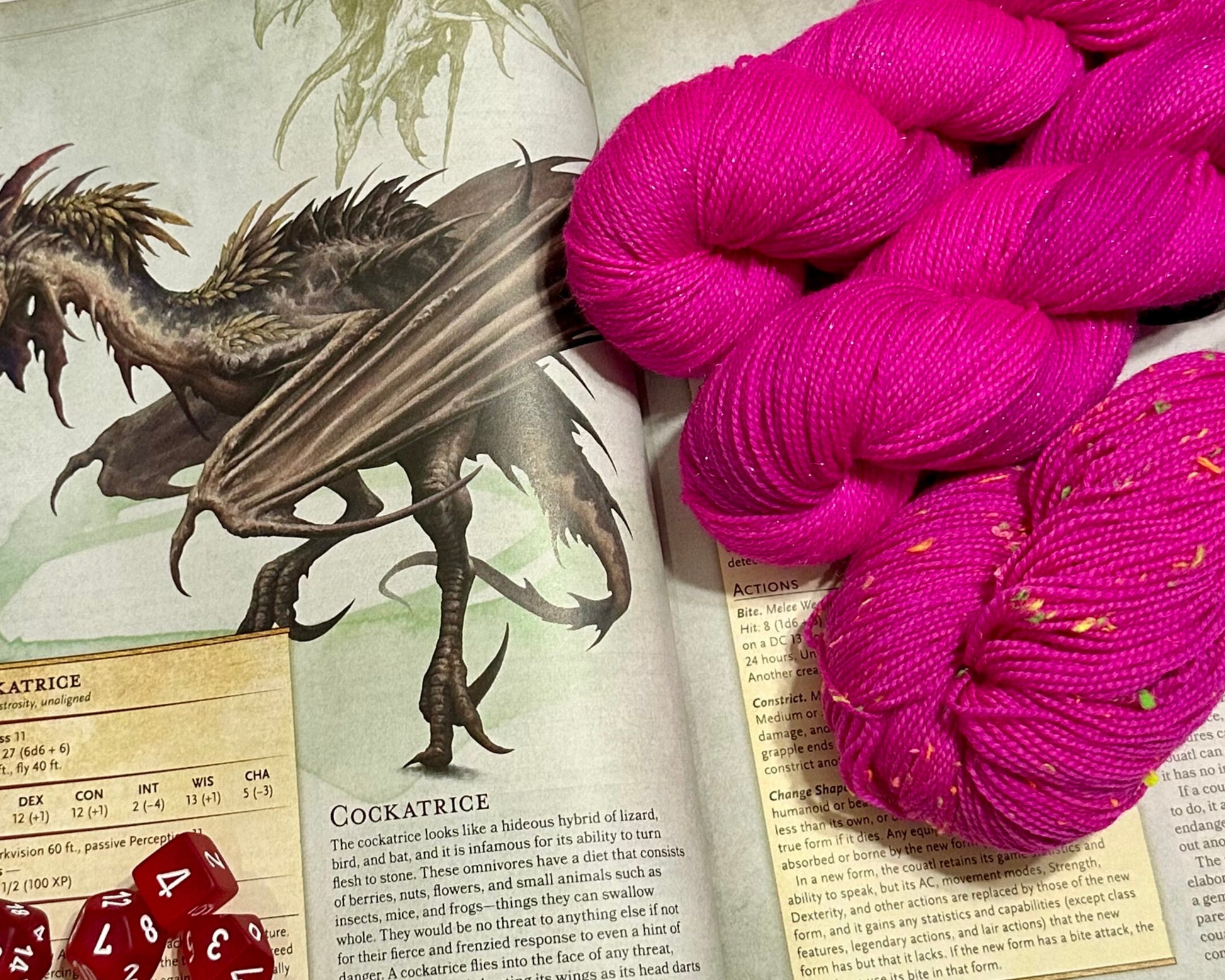 Pink yarn skeins on an open book with a dragon illustration