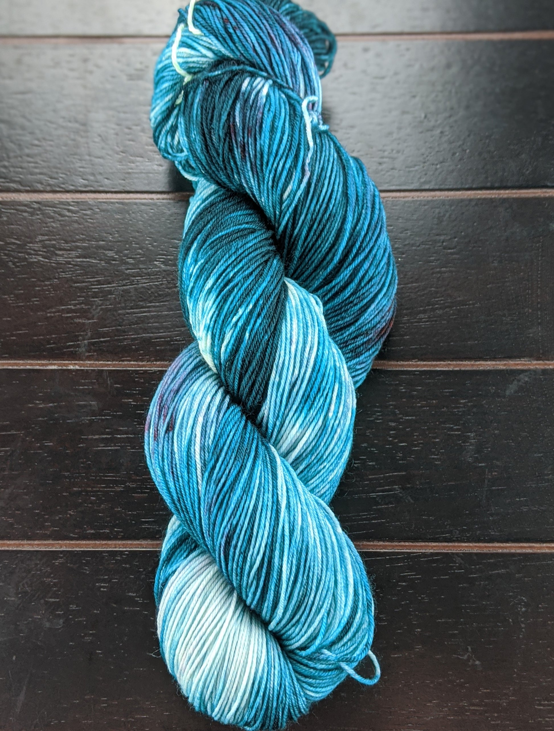 A skein of teal-colored yarn placed on a wooden surface.